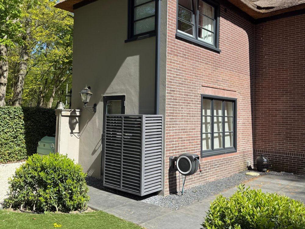 Buitenunit met luxe antraciet omkasting bij villa met rieten kap